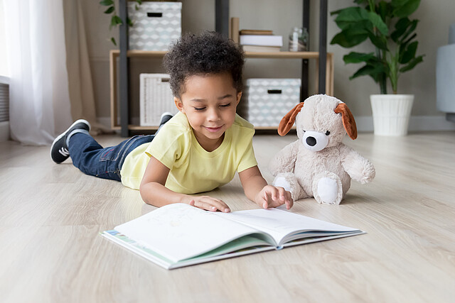 Adorable preschooler mixed race child boy reading book at home